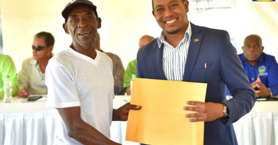 State Minister in the Ministry of Industry, Commerce, Agriculture and Fisheries, Hon. Floyd Green (right), presents a land lease document to Trevor Morris, former worker at Monymusk sugar factory in Clarendon. (JIS Photo)