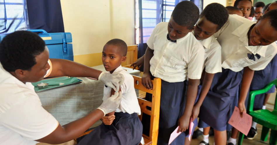 A young girl in Rwanda receives her HPV vaccination while her classmates nervously wait their turn. (PHOTO: © UNICEF/Laurent Rusanganwa)